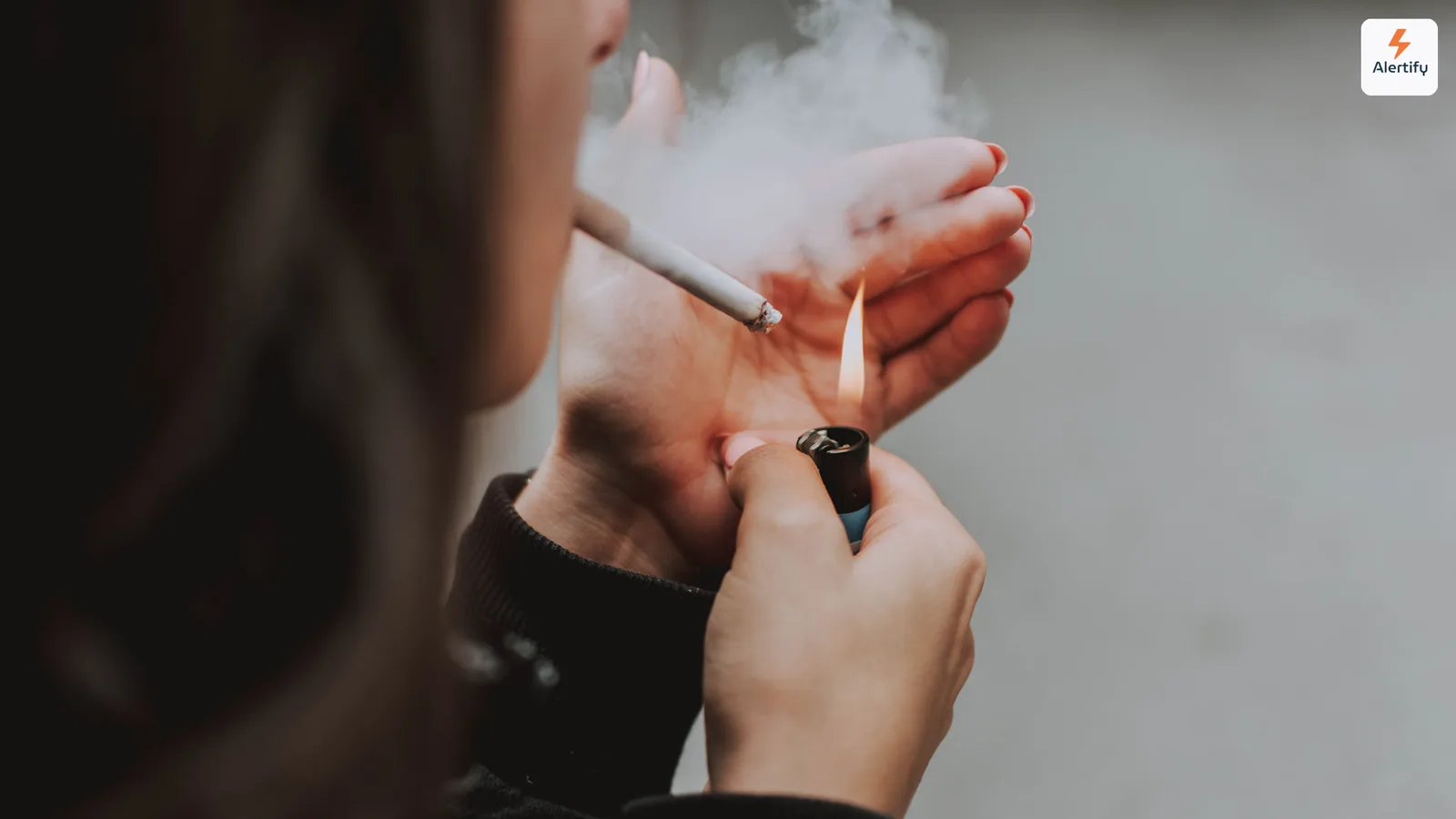 Pessoa a acender um cigarro dentro de casa com fumo a formar-se à volta das mãos