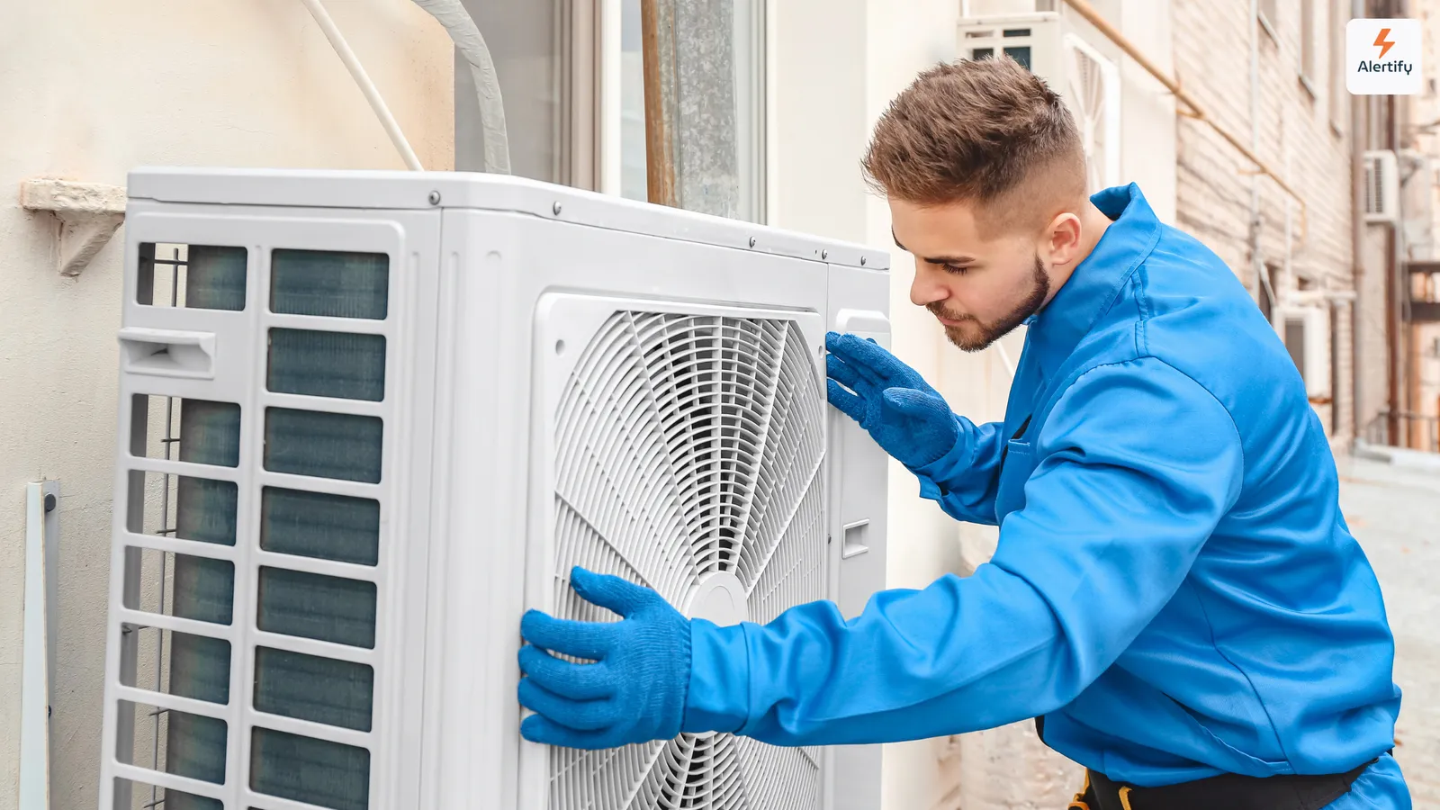 Técnico de AVAC de fato-macaco azul e luvas a fazer a manutenção de uma unidade exterior de ar condicionado
