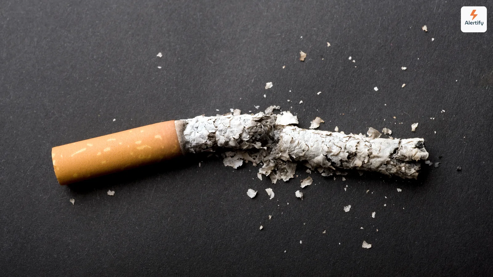 Cigarro partido ao meio com cinza espalhada sobre uma superfície escura